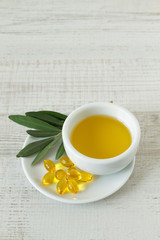 Close-up of bowl with olive oil, natural pills and olive branch kept on wooden table