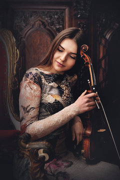Young girl embrace her violin sitting in an armchair
