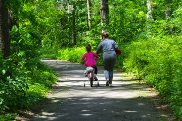 Obraz premium Dabushka and granddaughter ride a bicycle in the city park. May 28, 2017.