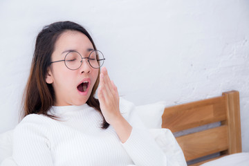 Beautiful asian woman waking up and yawn in bed in the bedroom, healthcare concept.