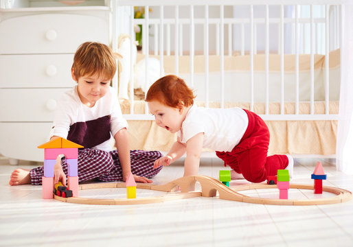 happy kids, brothers playing together with wooden toy railway in nursery room