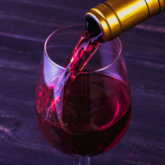 Pouring red wine into the glass against wooden background