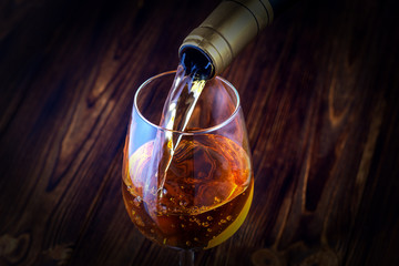 Pouring white wine into the glass against wooden background. Toned.