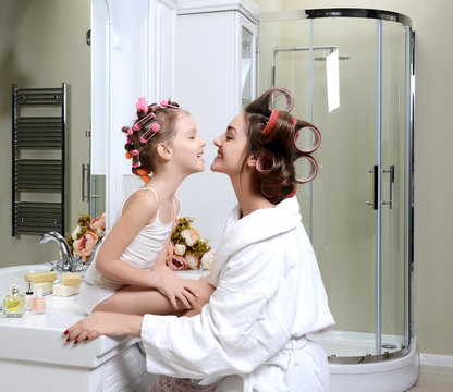 Young mother and daughter in curlers in a bath room happy smiling