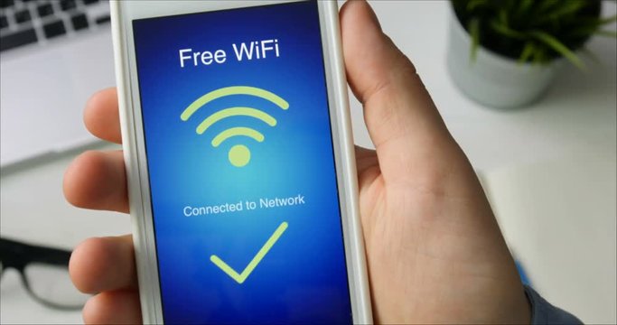 Man connects to free wifi network using his smartphone sitting at the desk