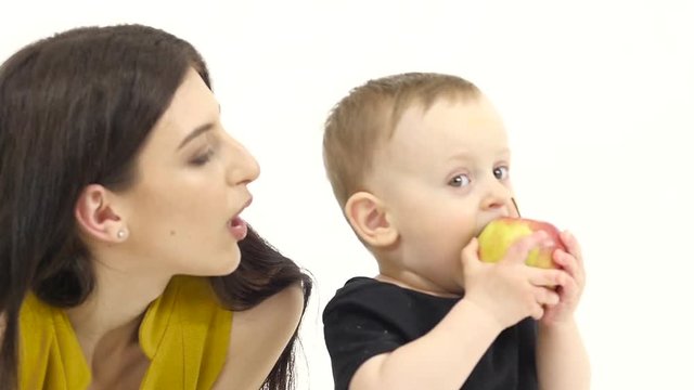Baby eats an apple, he likes it. White background. Slow motion