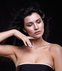 Fototapeta premium Portrait of a young brunette woman with long black streaming hair on black