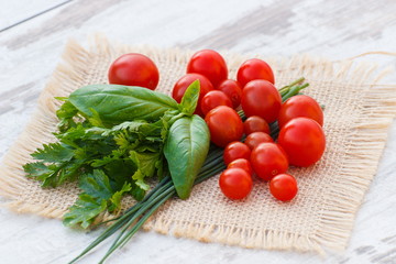 Red cherry tomatoes with green parsley and basil on jute canvas