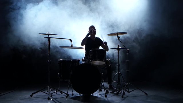 Energetic musician plays good music on drums. Black smoky background. Silhouette