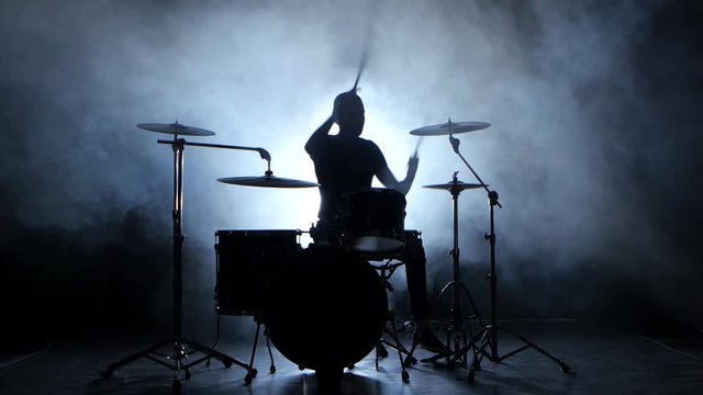 Drummer plays the melody on the drums energetically. Black background. Silhouette