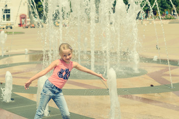 Little girl playing with water in city fountain.