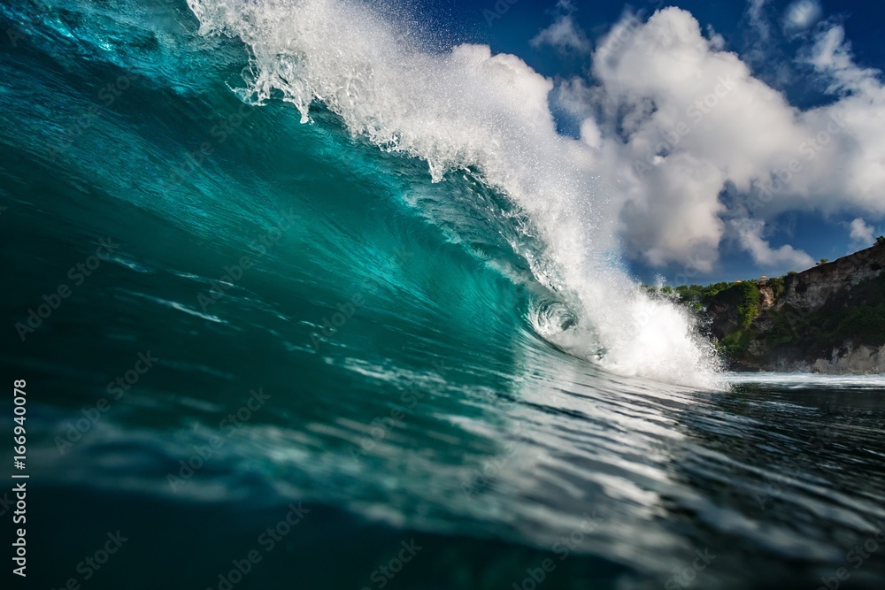 Wall mural blue ocean wave crashing near rocky wall
