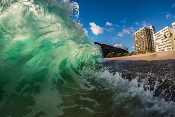 Big green wave crashing at shore near hotel at beach
