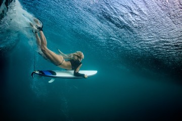 Fototapeta Blonde girl Surfer holding white surf board Diving Duckdive under Big Beautiful Ocean Wave. Turbulent tube with air bubbles and tracks after sea wave crashing. obraz