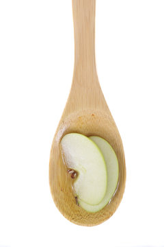 Apple cider vinegar and a slices of apple on a bamboo spoon.