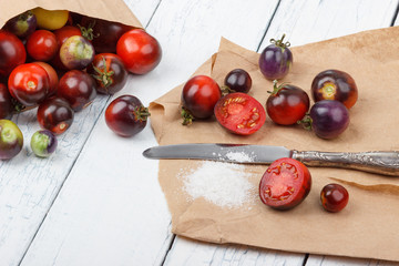 Different tomatoes in the paper bag on the white wooden background