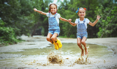 Happy funny sisters twins child girl   jumping on puddles in rubber boots