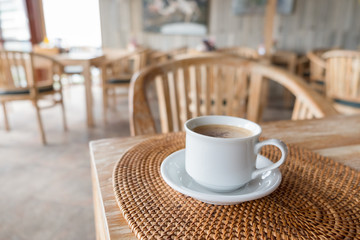 white cup of hot coffee on wooden table with morning sunlight in coffee shop, Bali, Indonesia