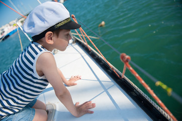 curious handsome little boy in a captain's hat peeking over the side of the boat