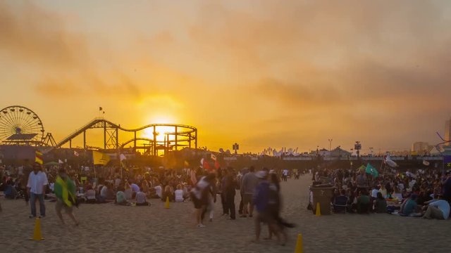 Cinematic 4K time lapse in motion (hyper lapse) on Santa Monica, California beach at sunset with the Santa Monic pier, ferris wheel, vacationers and clouds racing above.