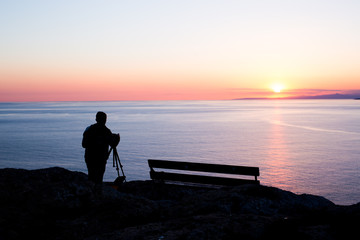 Fototapeta premium man photographer taking photos of sunset at the sea