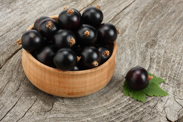 black currant in wooden bowl with green leaf on old wooden background