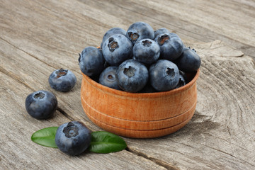blueberries with green leaf in wooden bowl on old wooden table background