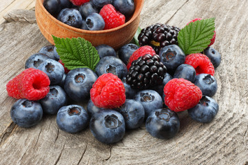 mix of blueberries, blackberries, raspberries in wooden bowl on old wooden table background