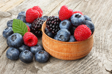 mix of blueberries, blackberries, raspberries in wooden bowl on old wooden table background