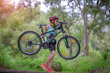 Fototapeta na wymiar woman carry mountain bike by holding frame body of bicycle cross over raceway in the rainforest