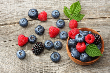 mix of blueberries, blackberries, raspberries in wooden bowl on old wooden table background