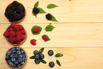 mix of blueberries, blackberries, raspberries in wooden bowl on light wooden table background. top view with copy space