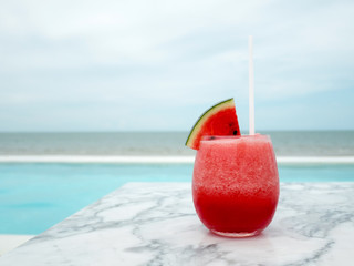 fresh watermelon smoothie in a glass jar on marble table near swimming pool,sea background