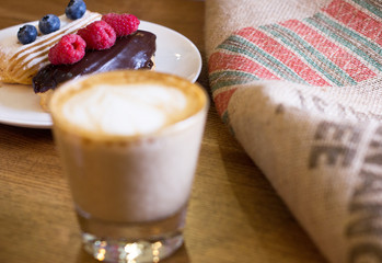 Cappuccino and cake with berries on table.