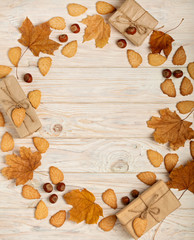 Flat lay frame of yellow leaves, cookies in the form of leaves, hazelnuts and gift boxes on a light wooden background.