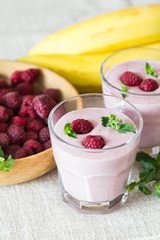 Two glasses of smoothies from banana and raspberries on a background of fruit