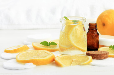 Refreshing lemon water facial tonic. Yellow citrus slices in jar, white cotton pads. Home beauty care remedies.