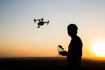 Fototapeta na wymiar quadrocopter drone with remote control. Dark silhouette against colorfull sunset.