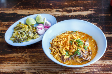 Curried noodle soup (Khao soi) with chicken meat and spicy coconut milk on wood table. Thai food cuisine northern style in Chiang Mai, Thailand.