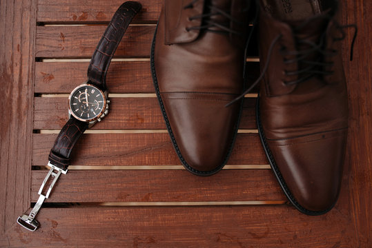Expensive man wrist metal watch with leather strap and shoes on wooden background