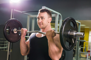 Naklejka na ściany i meble Strong and handsome man lifting weights a barbell in a gym