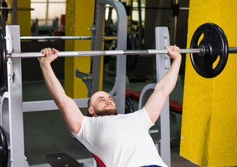 Brutal athletic man pumping up muscles on bench press. Sport, bodybuilding, training and people concept