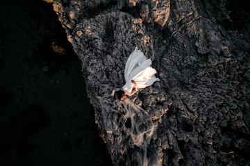 beautiful and young bride in white dress lying on big stone