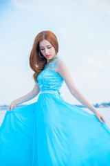 Fototapeta na wymiar Beautiful girl in light blue bright clothes, pure accessories and makeup, relax mood, at warm day on a yacht. Evening dress and stylish photography near sea. Beauty idea. Stunning young redhead woman