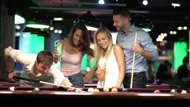 two happy young couples playing billiard together

