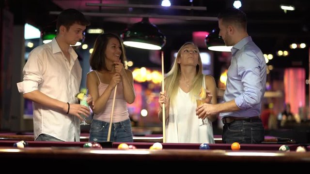 young woman drinking cocktail and playing billard with her friends

