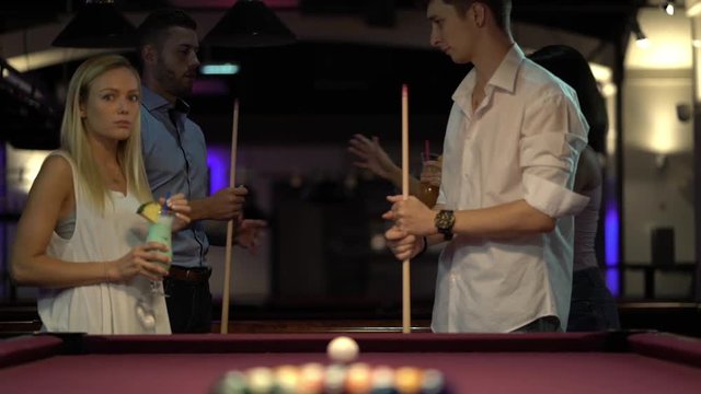 two young couples playing billiard together, man starting game
