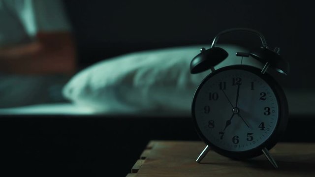 Man laying alone in bed at night, low key, selective focus on alarm clock