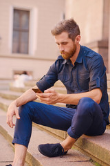 Fototapeta premium A man sits on a step and using a smartphone.