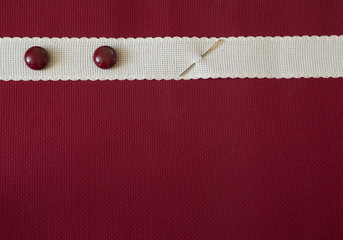 Red and natural canvas colors, red buttons and a needle. Things for needlework. Background for handmade with space for text.